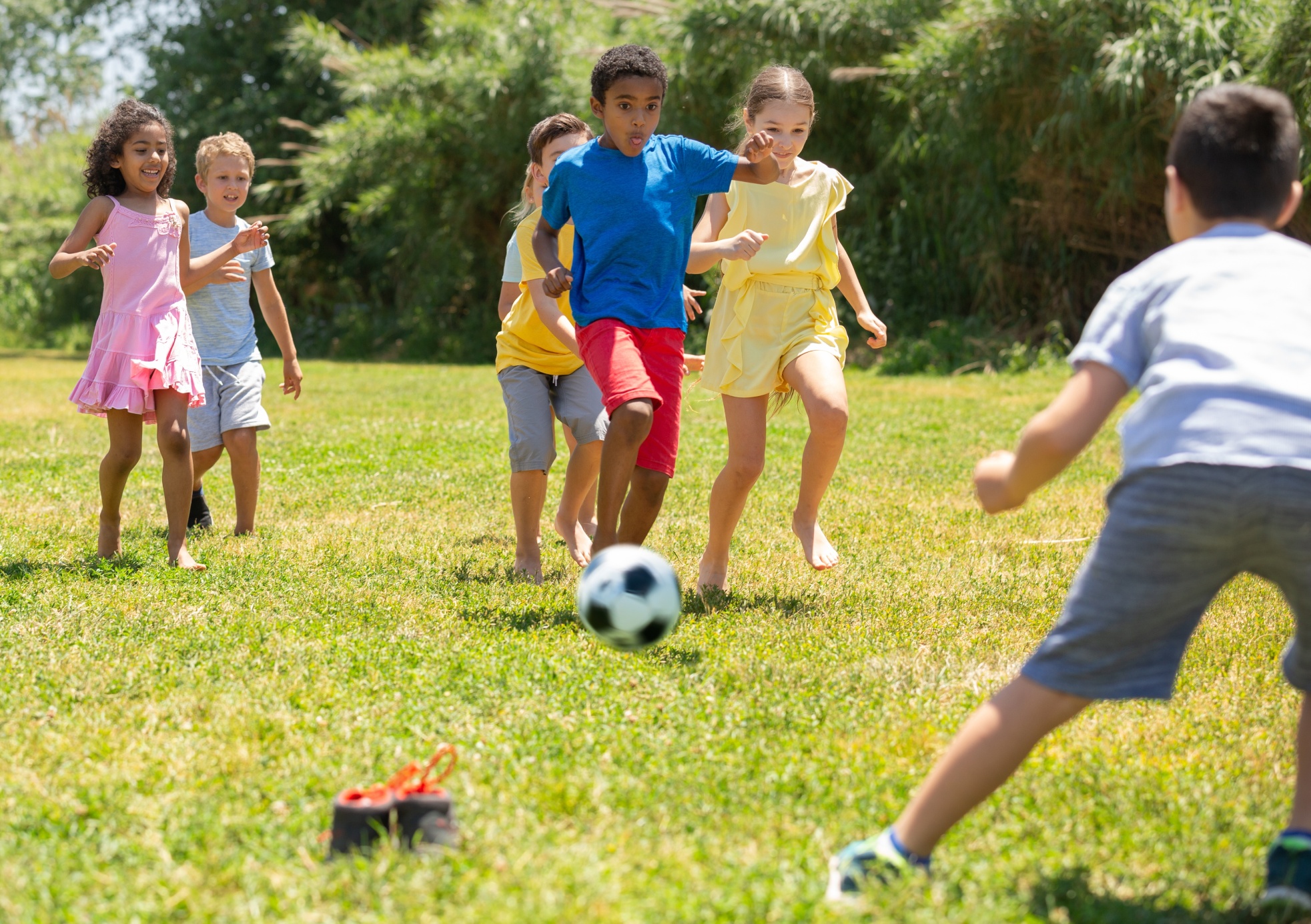 Group of happy schoolchildren playing football together in park