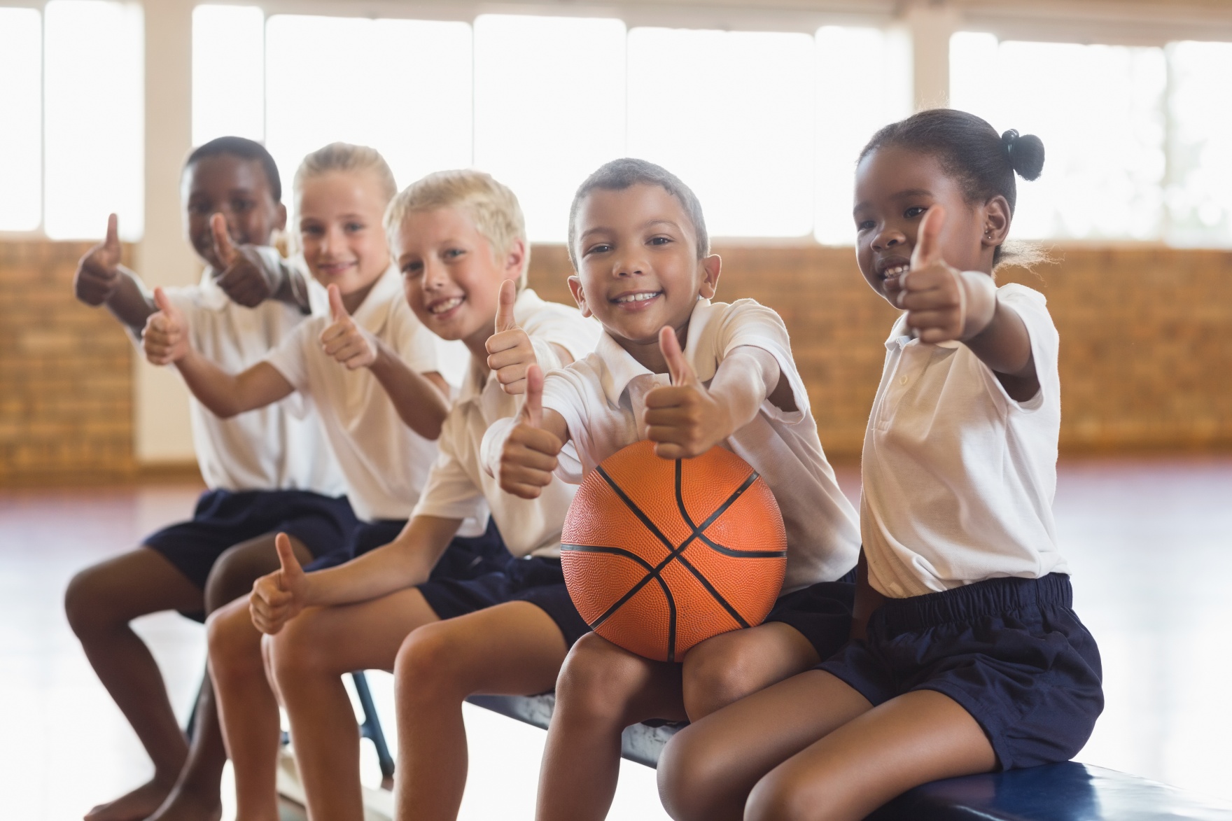 Smiling students with basketball showing thumbs up in school gym